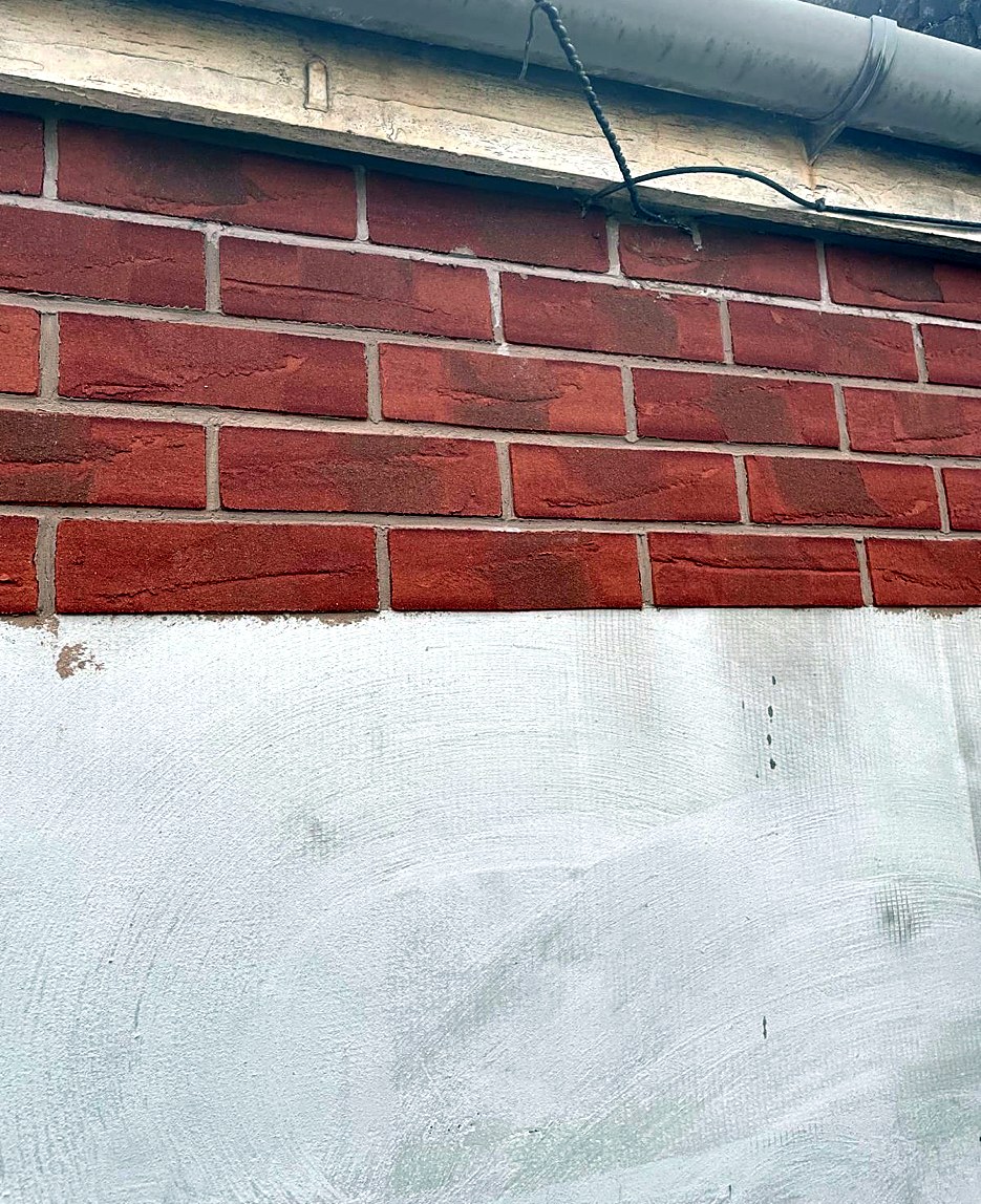 Red brick slips being applied above a rendered wall