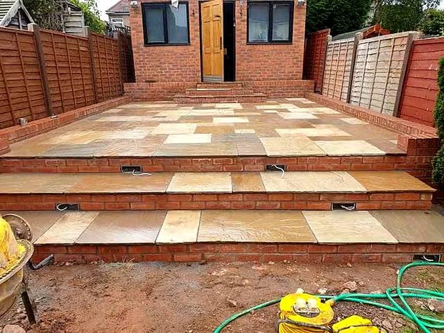Raised sandstone patio with brick-edged steps to a garden room in the Wolverhampton area